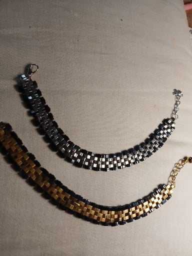 Two beaded necklaces, one black and silver, the other gold and black, on a beige surface.